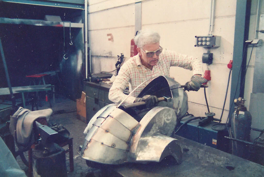 Dino 2000, Werkstattfoto: Bearbeitung eines gebogenen Metallteils an der Werkbank