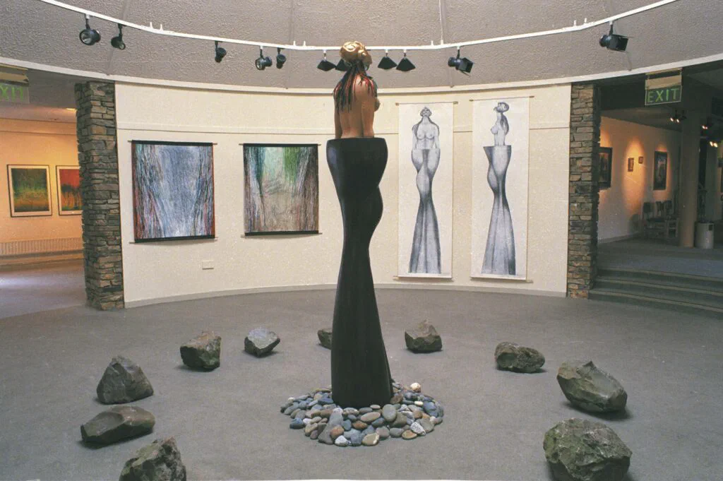 Meadhbh, Rückansicht im Ausstellungsraum, Skulptur, Holz/Bronze/Leder