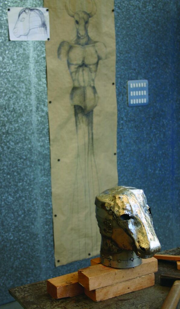 Minotaurus 2, Werkstattfoto: Kopf auf der Werkbank vor Entwurfszeichnungen an der Wand